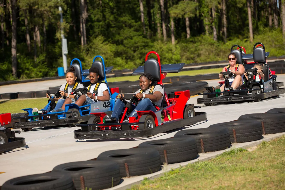 A lively exterior shot of a go-kart racetrack where racers compete, surrounded by friends and family cheering them on. The energy and camaraderie on display make it ideal for illustrating group bonding activities.
