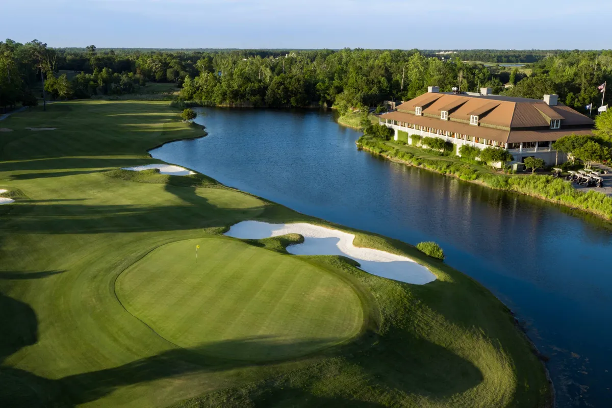 A lush golf course featuring rolling greens, sand traps, a shimmering lake, and a charming clubhouse. The scene is tranquil, hinting at leisurely days and the opportunity for complimentary golf as part of your stay.