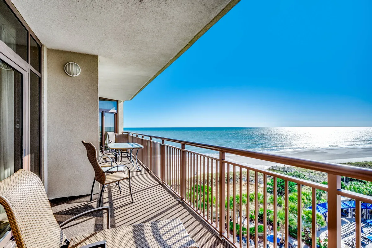 An expansive covered balcony overlooking the ocean, complete with comfortable seating arrangements and a table. The setting is tranquil and perfectly suited for morning coffee rituals or sunset toasts with the sound of the surf below.