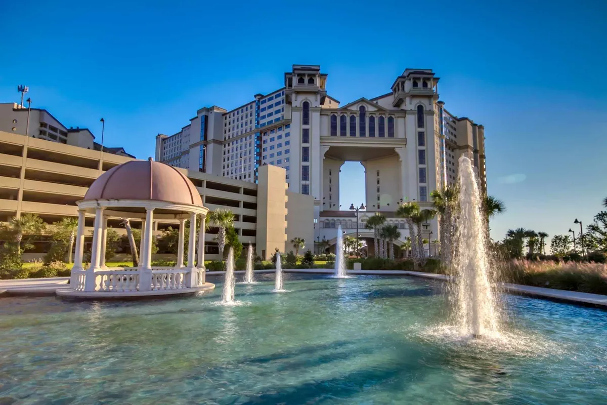 The image features a beautiful exterior scene with a gazebo, decorative fountains, and a large, elegant building reflected in the water. The area exudes luxury and serenity, perfect for social gatherings or peaceful relaxation, with lush landscaping enhancing the upscale atmosphere.