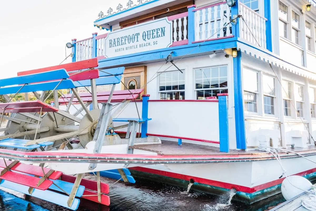 An exterior view of the colorful Barefoot Queen riverboat, with its classic paddlewheel and signage, inviting guests to imagine scenic sightseeing cruises and social gatherings on the water.