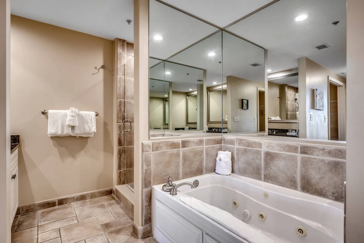 A luxurious bathroom featuring a whirlpool bathtub, reflective mirrors, and a tiled shower area. The ambiance is tranquil and rejuvenating, underscoring the en-suite bath experience and offering a retreat for relaxation and self-care.