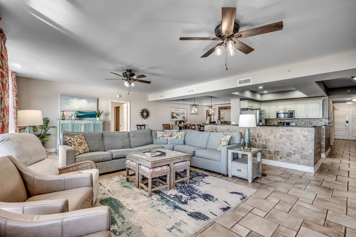 A spacious living room featuring a large sectional sofa, a colorful area rug, a coffee table with magazines, and decorative wall art. The space is arranged for comfort and social gatherings, creating an inviting atmosphere for movie nights or group conversations.