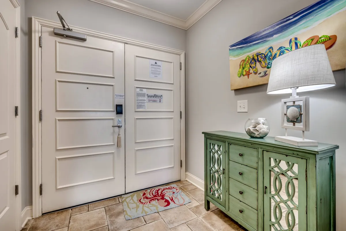 This image presents a welcoming entryway featuring double doors, a cheerful green accent table, framed coastal artwork, and a table lamp. The space is bright and inviting, setting the tone for a relaxed stay at North Beach Towers.