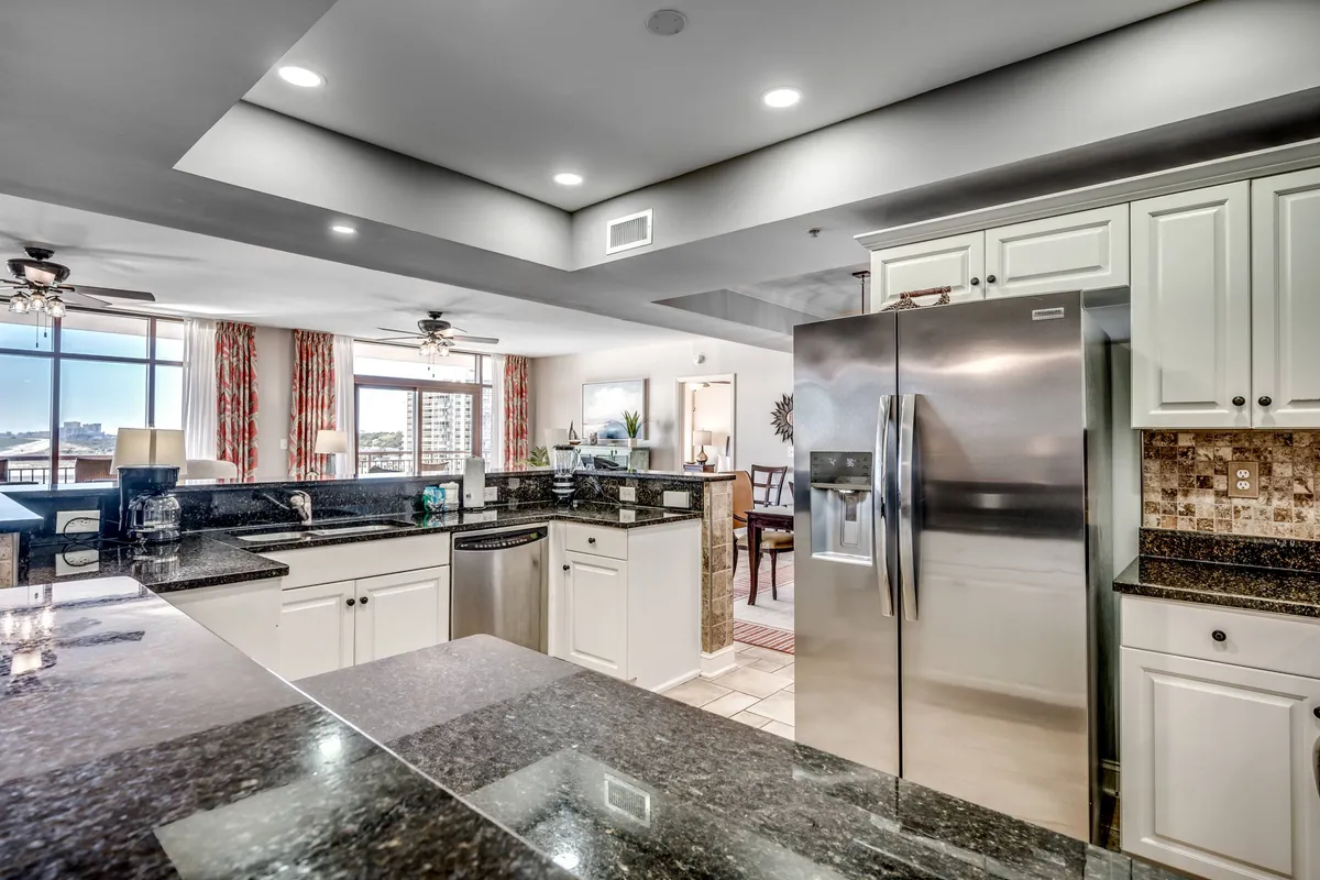 A stylish kitchen equipped with granite countertops, stainless steel appliances, and large windows dressed with decorative curtains. The kitchen is designed for both cooking and socializing, with inviting spaces for guests to gather.
